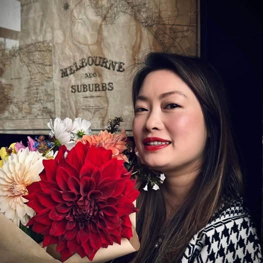 Linh holding a bouquet of dahlias in front of an old map of Melbourne