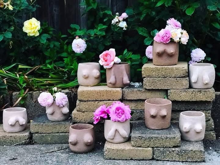 Blush planters with sculpted forms, filled with roses on garden bricks