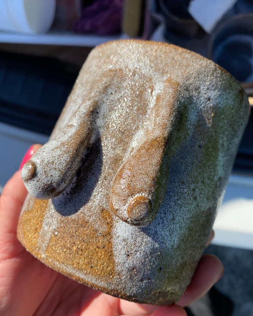 A speckled stoneware cup with two sculpted forms, held in a hand