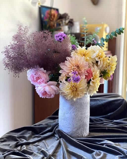 A speckled vase with dahlias and smoke bush